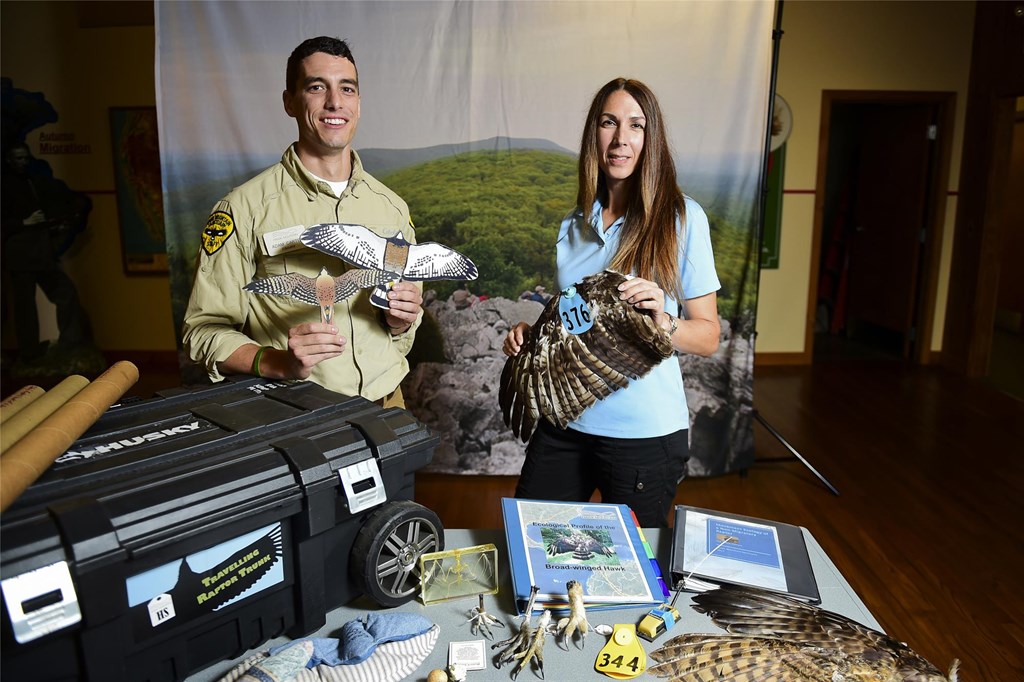 Two educators posing with cut out raptor silhouettes, wings, lesson plans, and other teacher materials