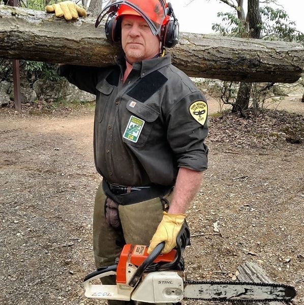 Todd Bauman in action, holding a tree log and chainsaw