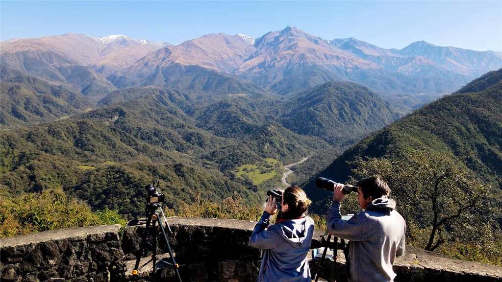 Fer and Emi look out with binoculars over a mountain landscape